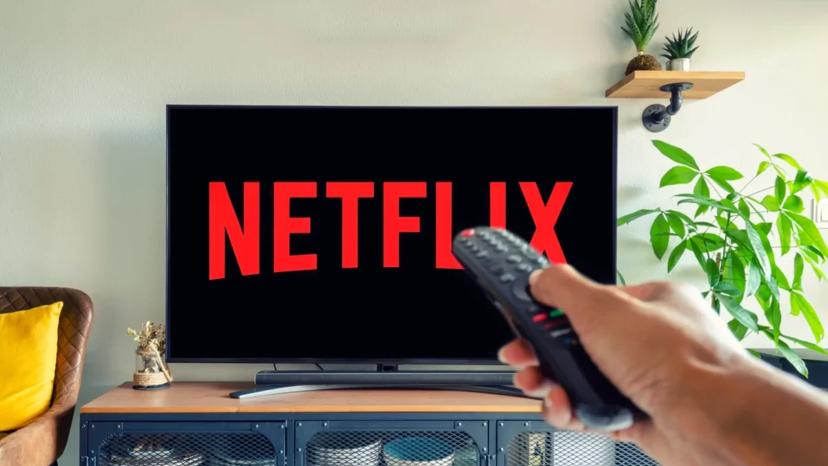 Logo Netflixu na televizi a muž s ovladačem v ruce