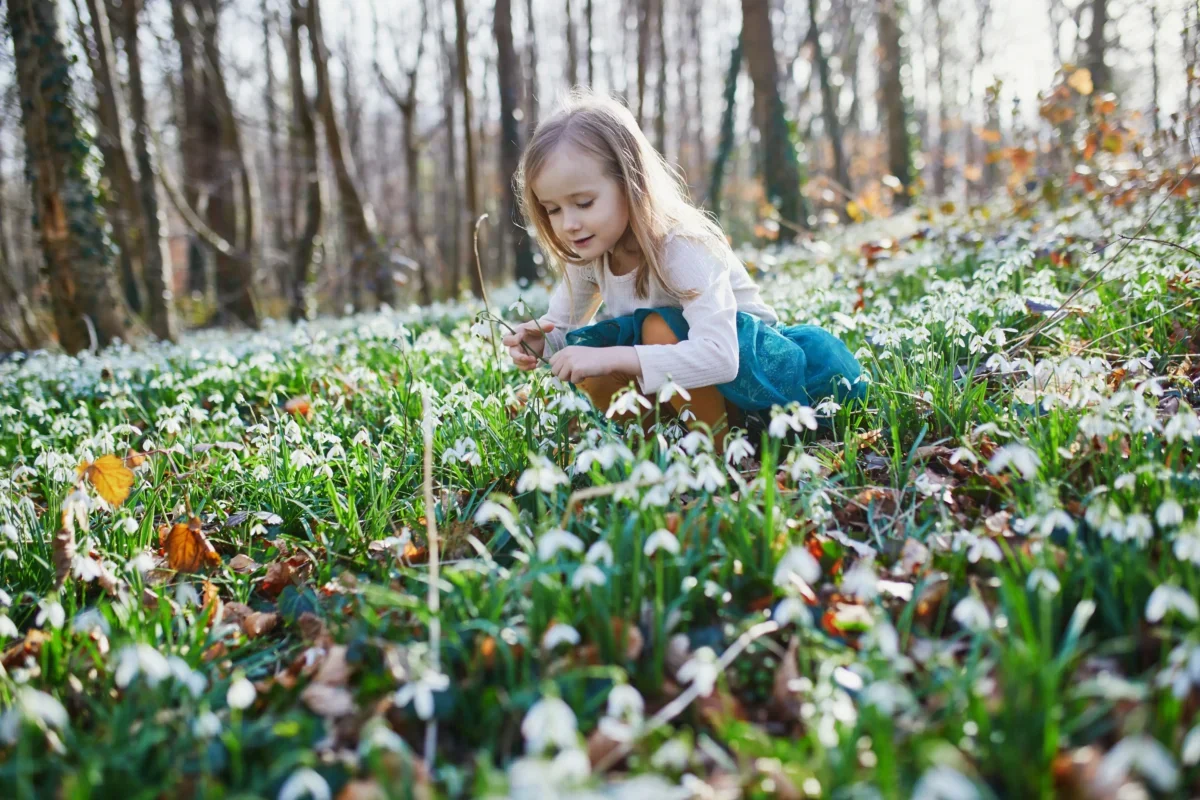 Holčička klečí mezi rozkvétajícími květinami.