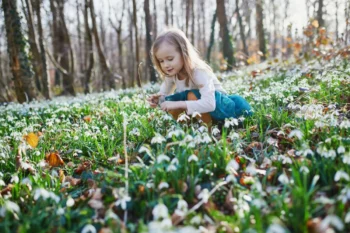 Holčička klečí mezi rozkvétajícími květinami.