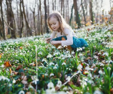 Holčička klečí mezi rozkvétajícími květinami.