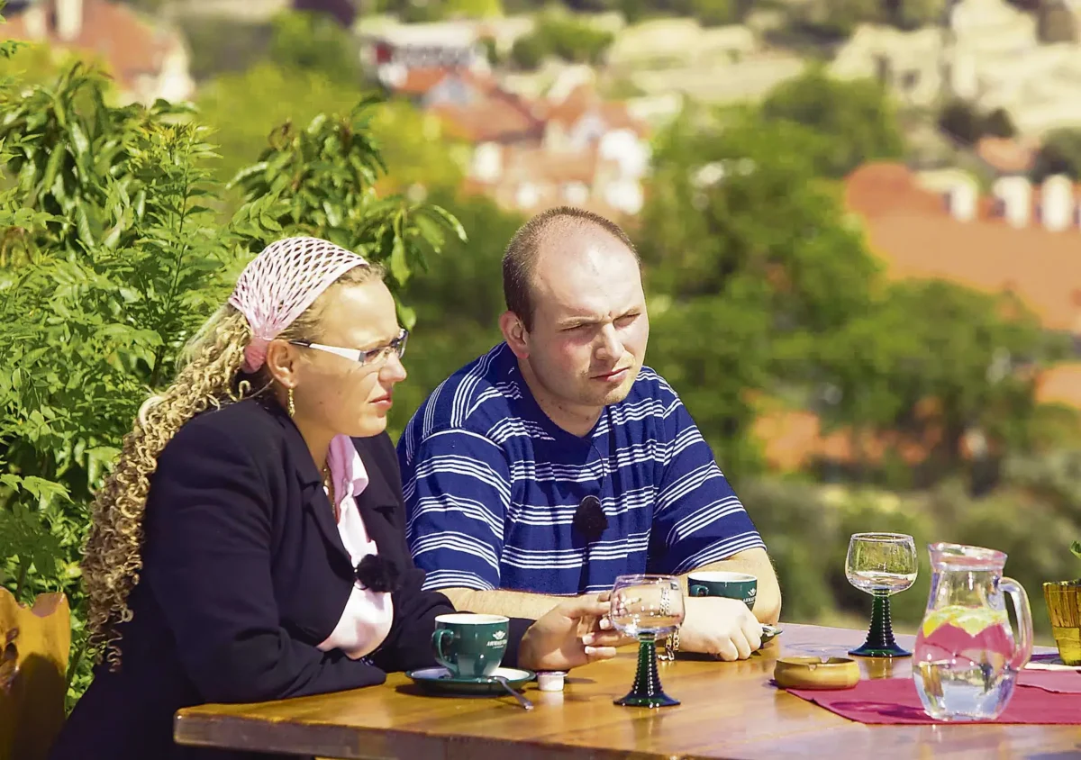 profimedia-0157456589 | TVGURU.cz Muž a žena sedí u stolu.