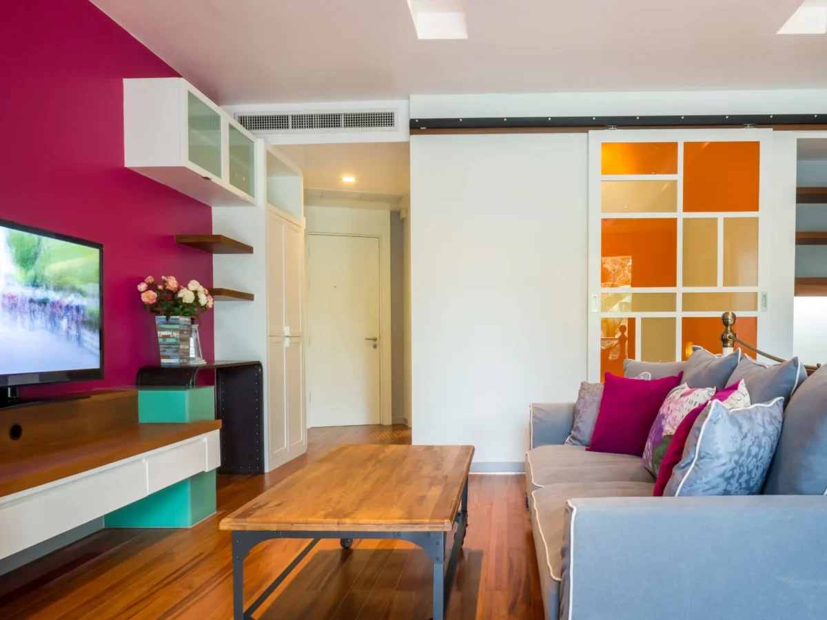 Naproti růžové stěně s televizí stojí gauč.