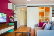 Naproti růžové stěně s televizí stojí gauč.