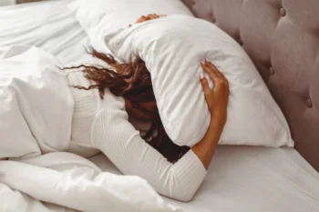 Žena si polštářem zakrývá hlavu.