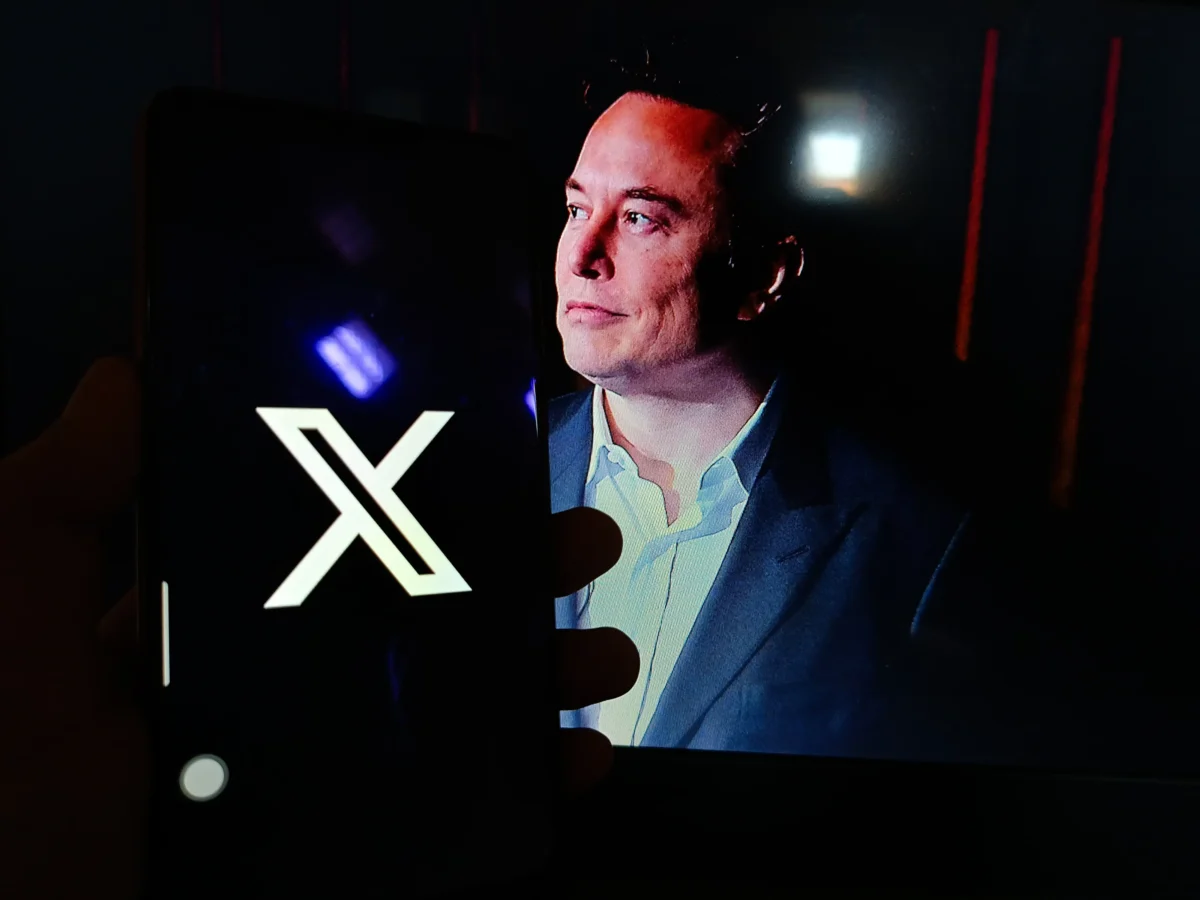 Na mobilu je spuštěné X a v pozadí je Elon Musk. 