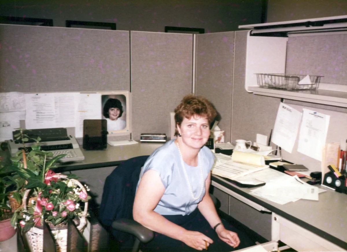 shutterstock_2670570197 | TVGURU.cz Žena sedí v práci u stolu.