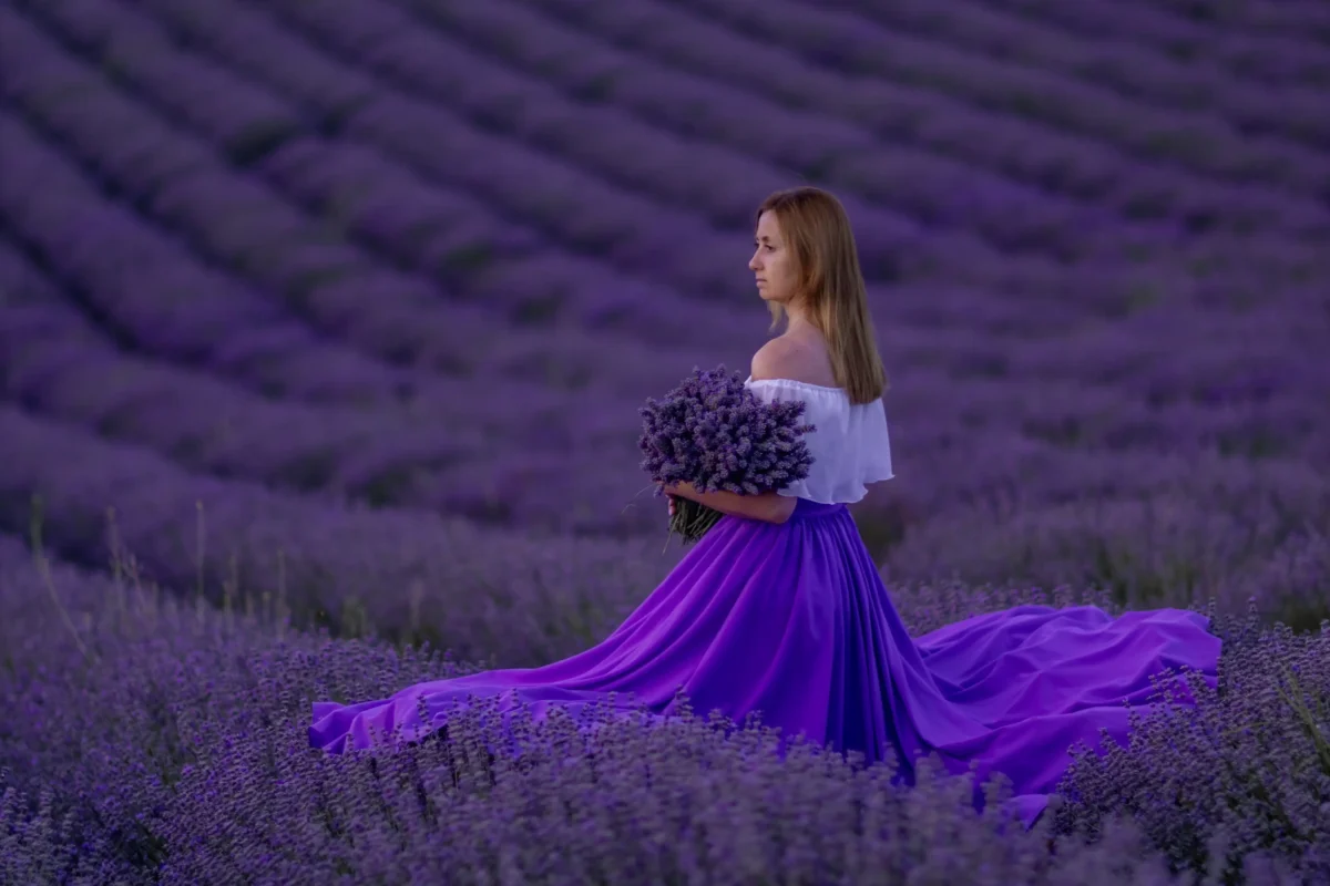 Žena ve fialových šatech stojí mezi levandulí. 
