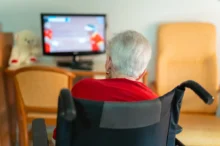 seniorka na vozíku sleduje televizi