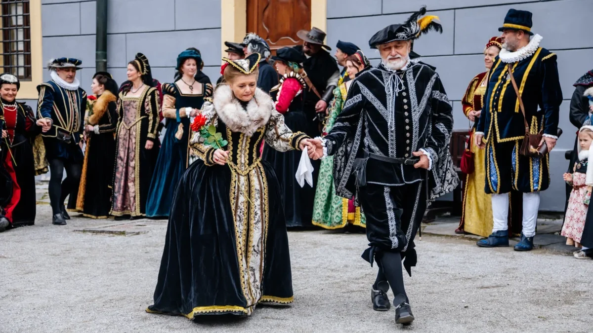 Dobově oblečení herci kráčí po nádvoří.