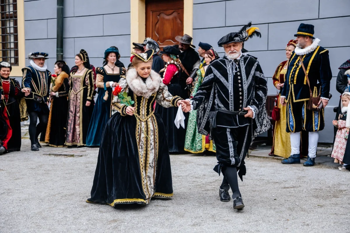 Dobově oblečení herci kráčí po nádvoří.