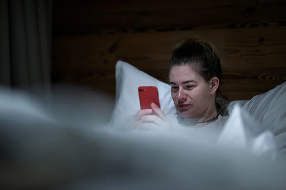 Žena se v posteli dívá do telefonu. 