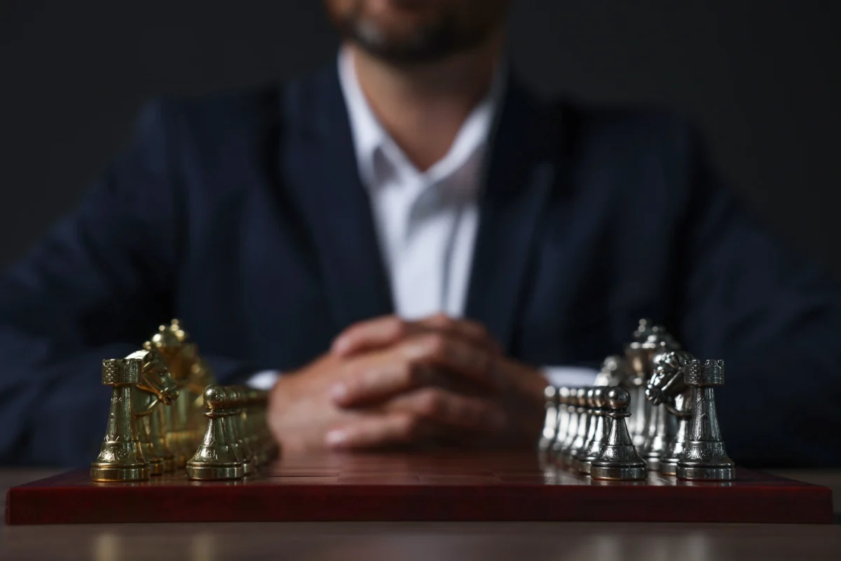 Muž sedí u stolu, na kterém jsou šachy. 