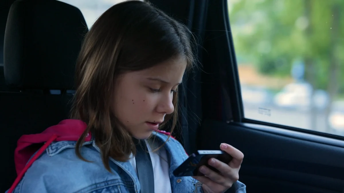 Holčička se v autě dívá do telefonu. 