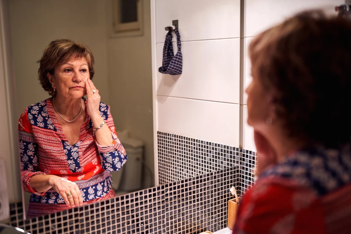 Stará žena se pozoruje v zrcadle. 