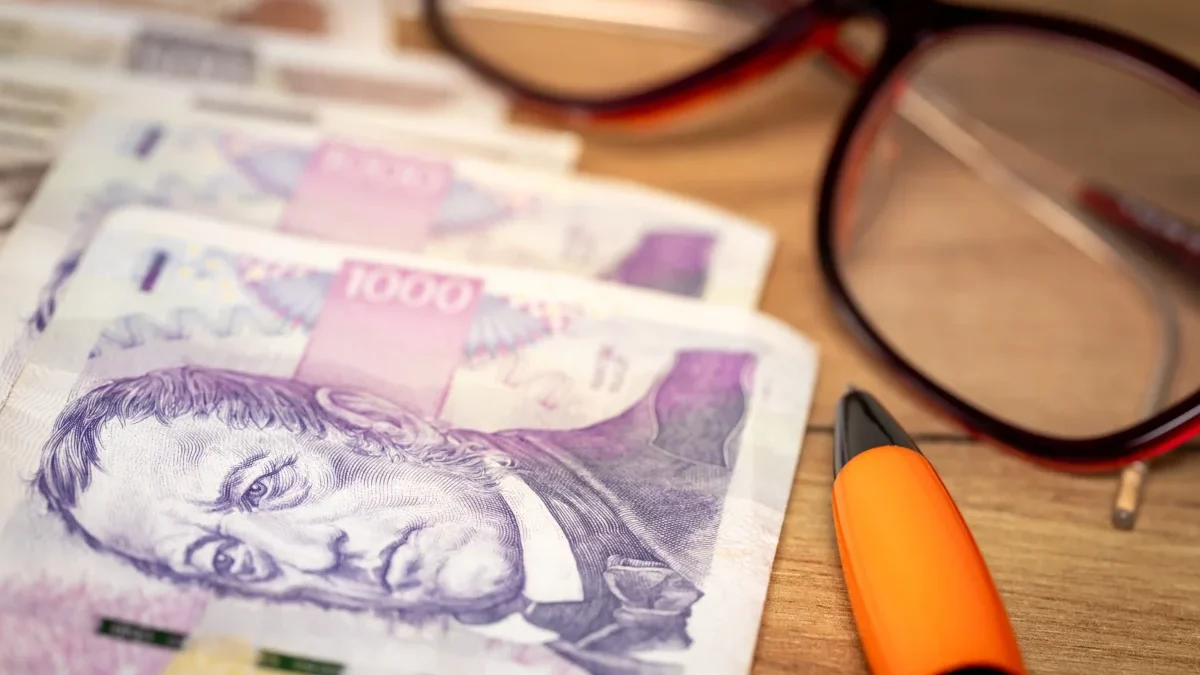 Na stole leží peníze, propiska a brýle.