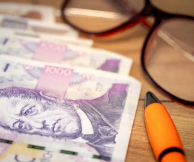 Na stole leží peníze, propiska a brýle.