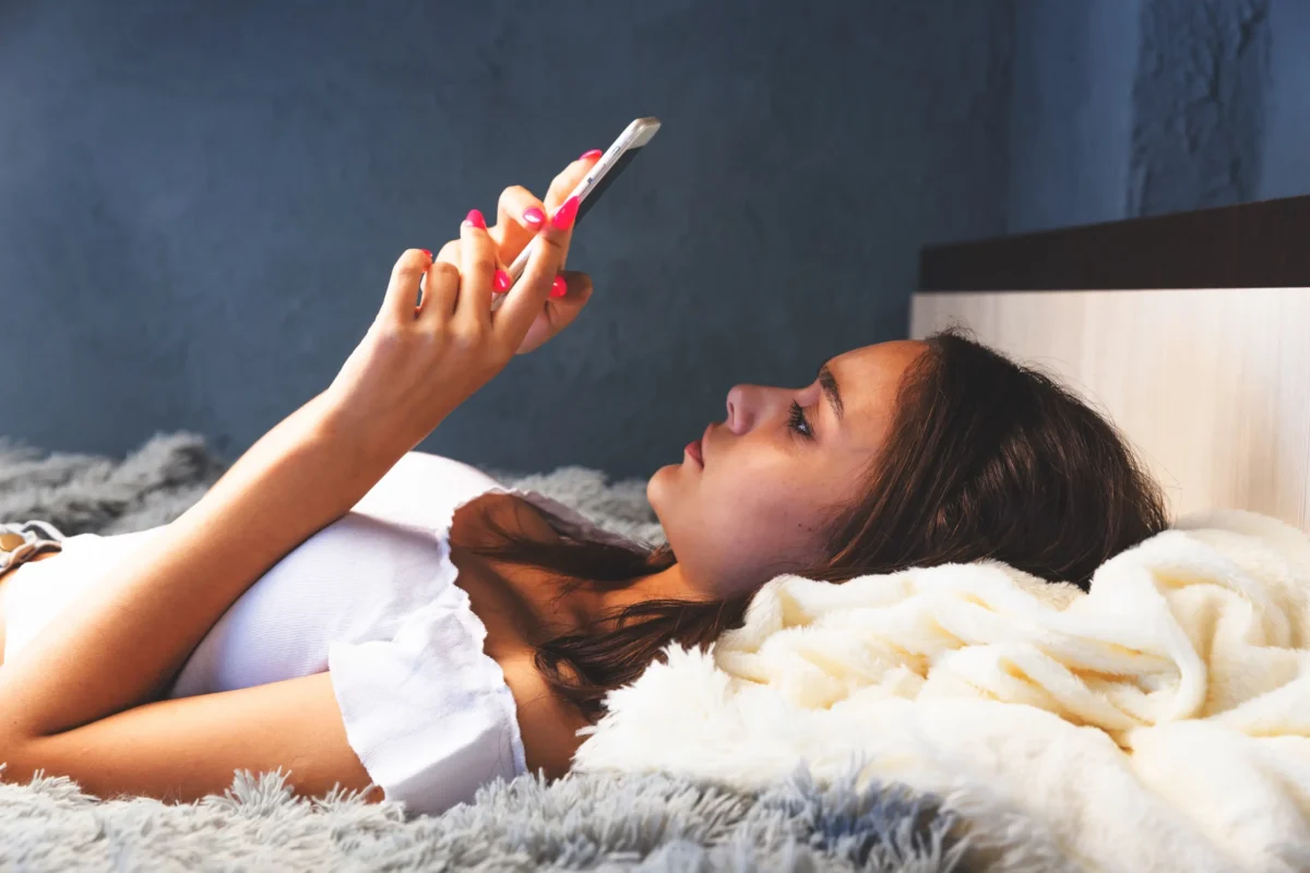 Slečna leží s telefonem na posteli.