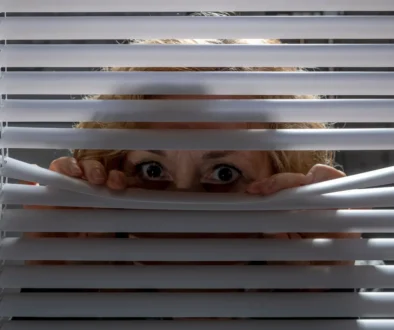 Žena vykukuje za žaluziemi.