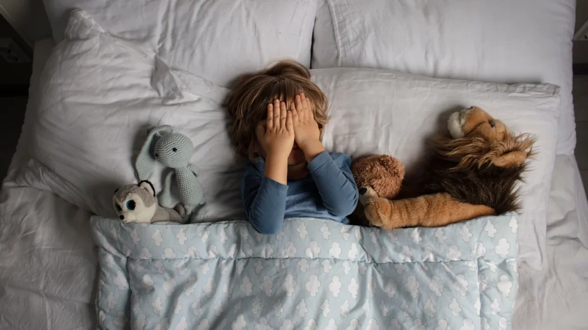 Chlapec leží v posteli a zakrývá si oči.