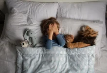 Chlapec leží v posteli a zakrývá si oči.