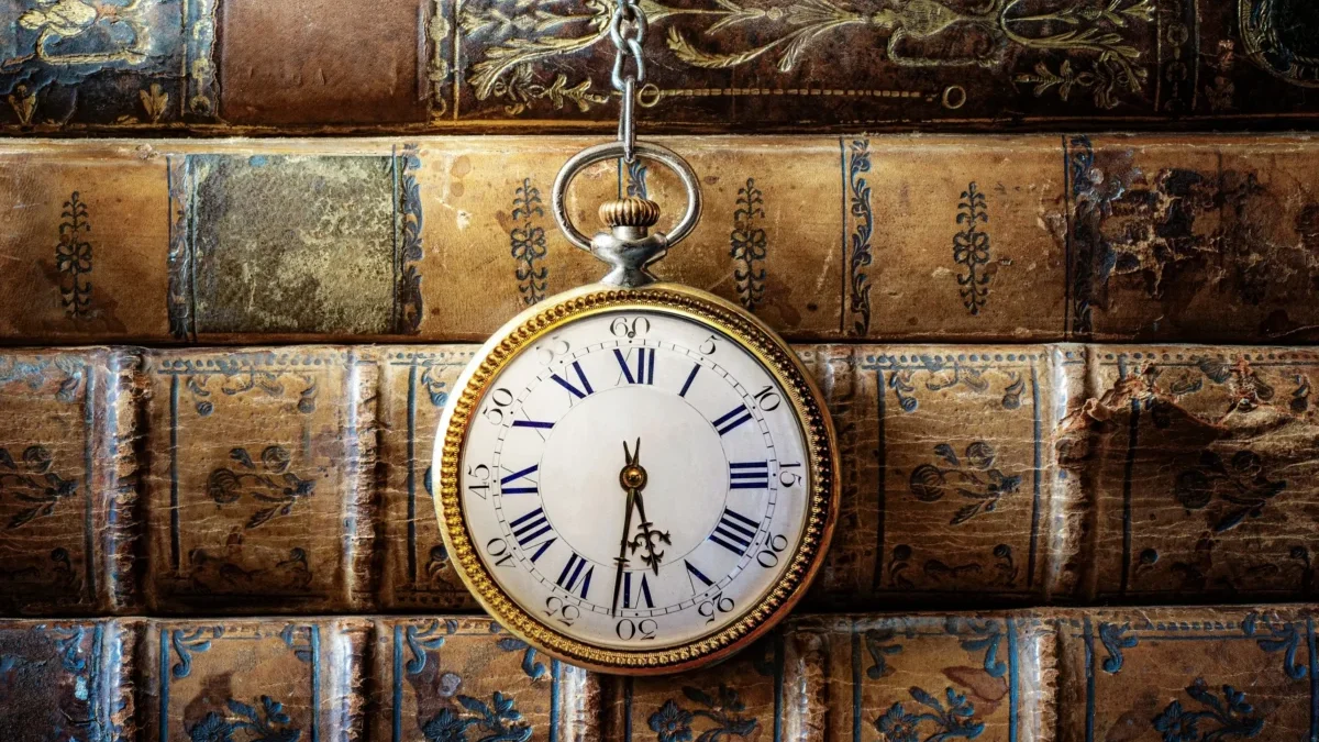 Před starými knihami visí hodiny.