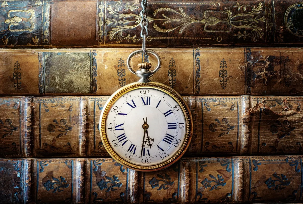 Před starými knihami visí hodiny.