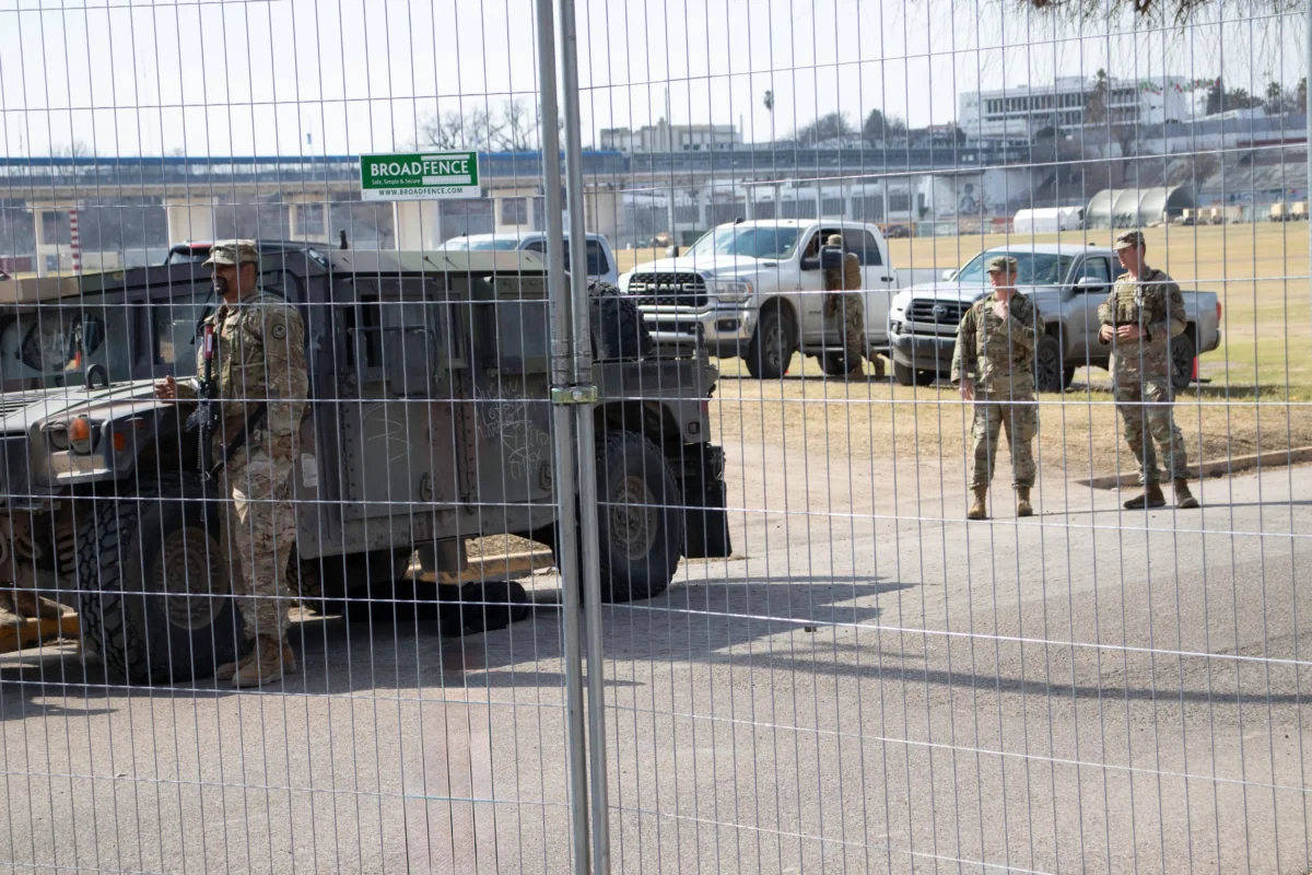 shutterstock_2425531977-2 | TVGURU.cz Za pletivem stojí vojáci a auta.