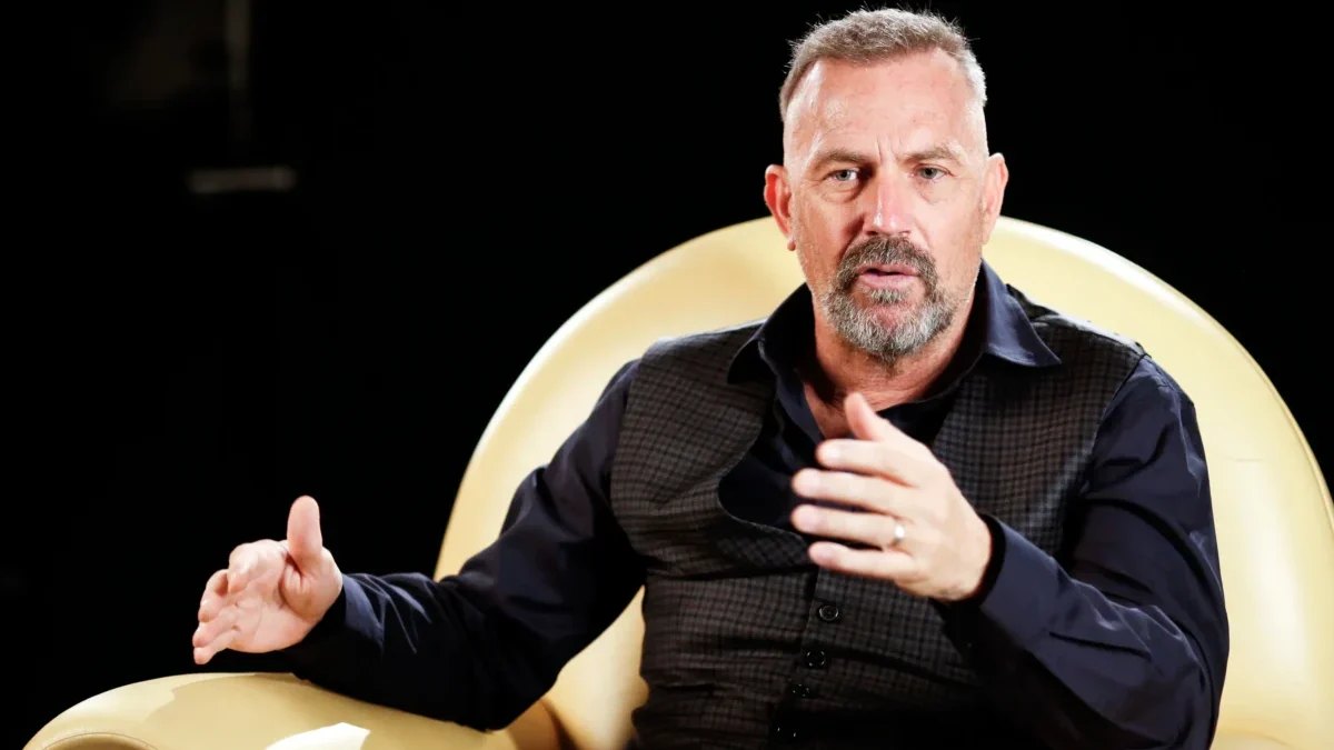 Kevin Costner sedí v křesle.