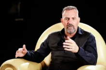 Kevin Costner sedí v křesle.