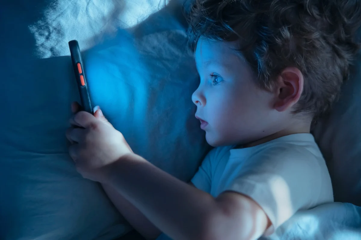 Chlapeček leží v posteli a kouká se do telefonu. 