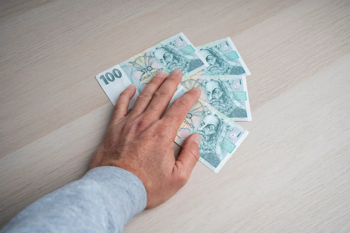 Člověku pod rukou vykukují bankovky. 