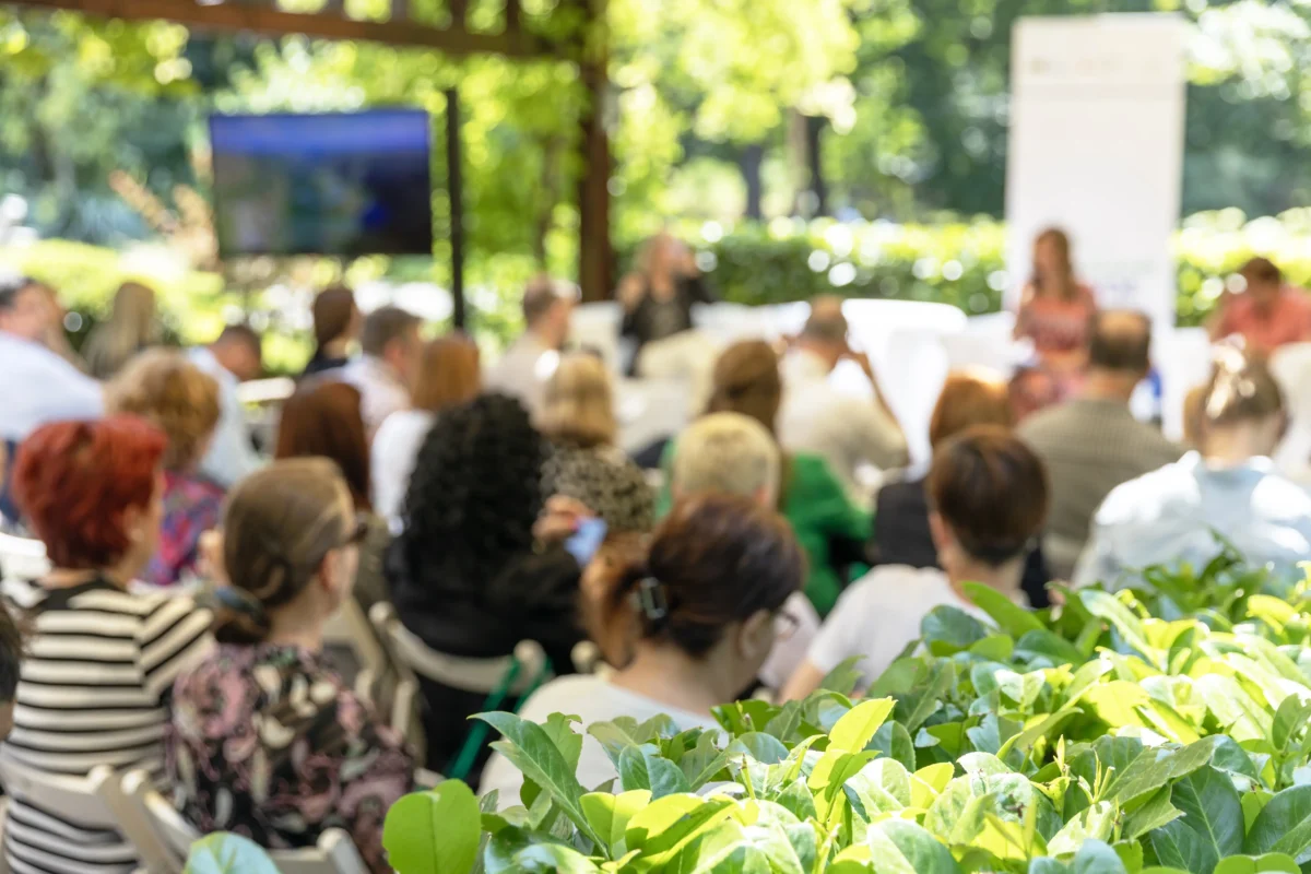 Lidé sedí venku za křovím. 