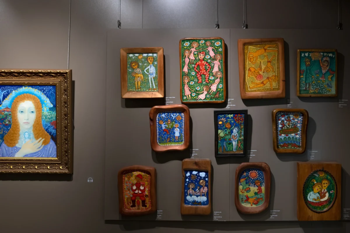 Na stěně visí několik obrazů naivního umění.