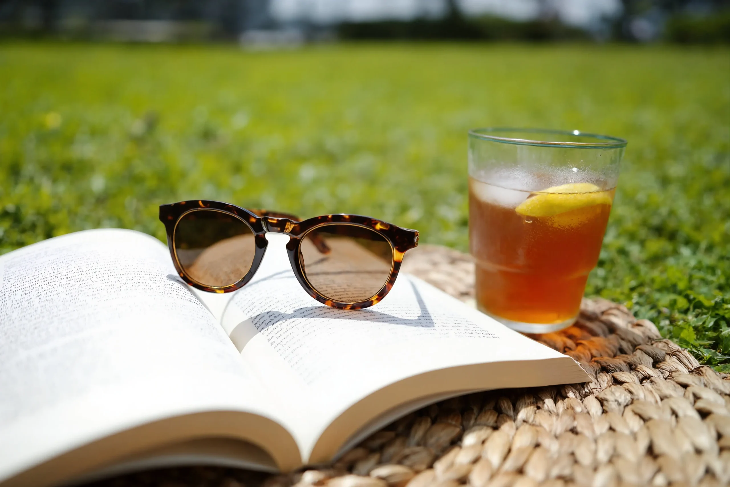 Kniha, sluneční brýle a pití s ledem položené na trávě v létě 