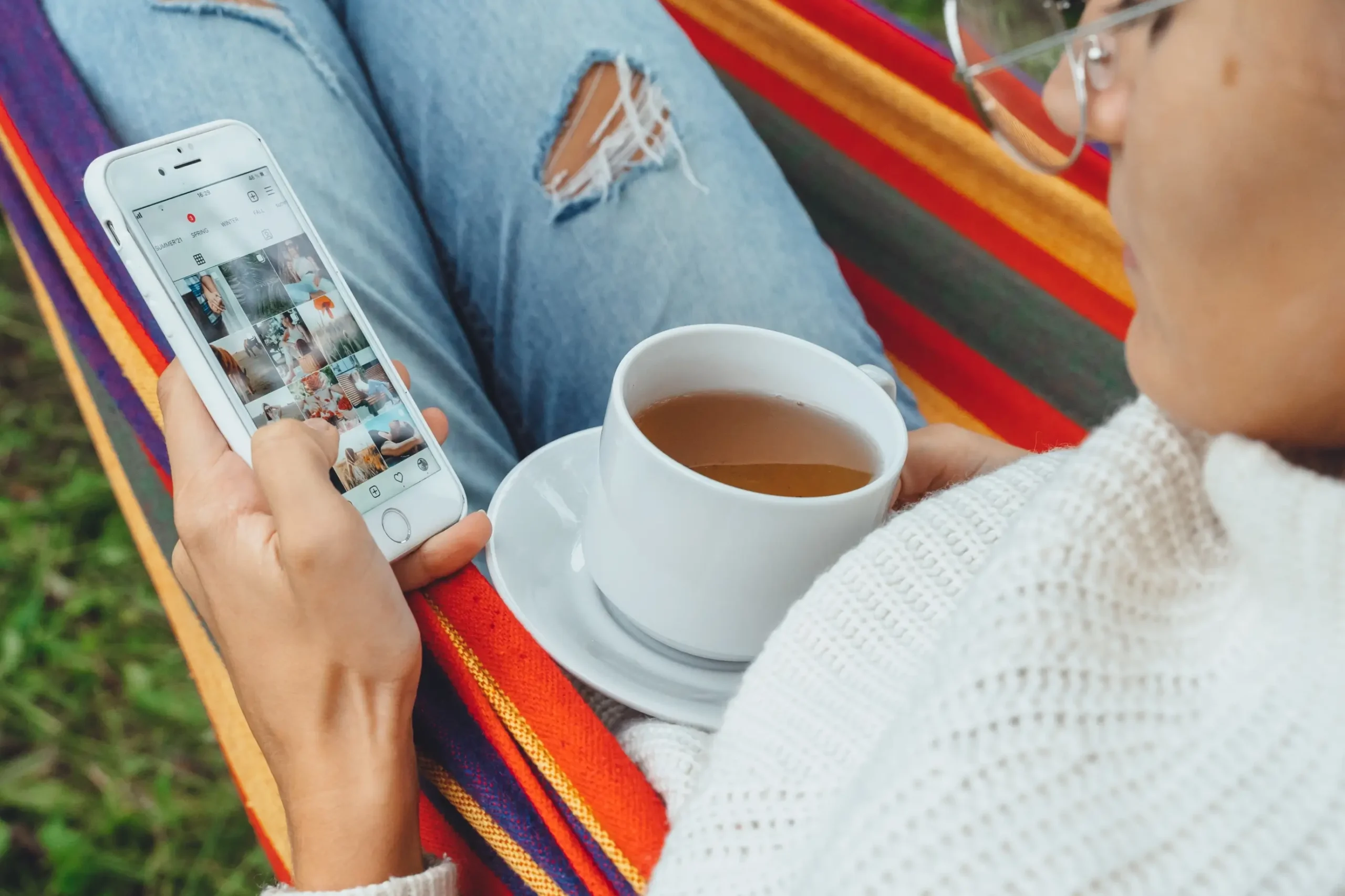 Žena projíždí na mobilu Instagram a má na klíně hrnek.