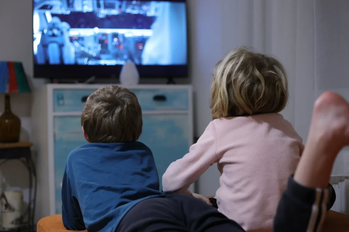 Děti leží u televize.