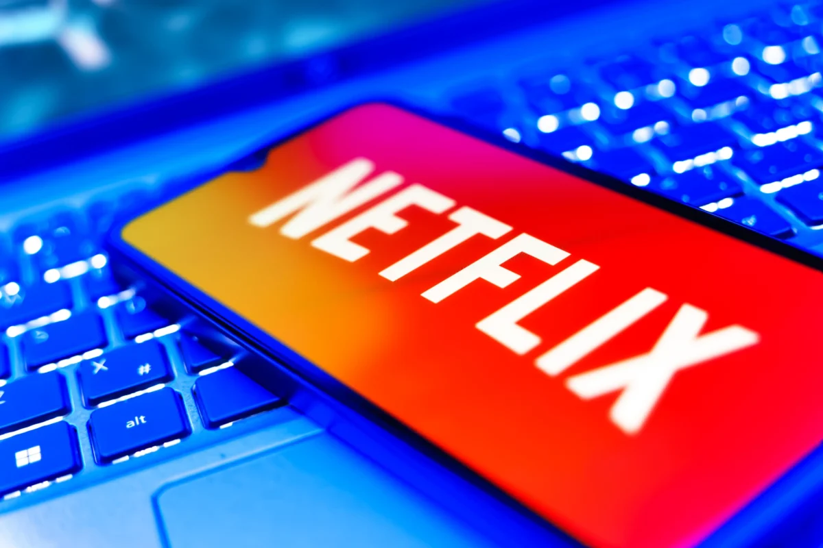 Na notebooku leží mobil s Netflixem.