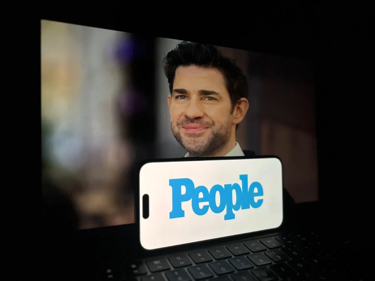 Před notebookem je položený mobil s nápisem People.