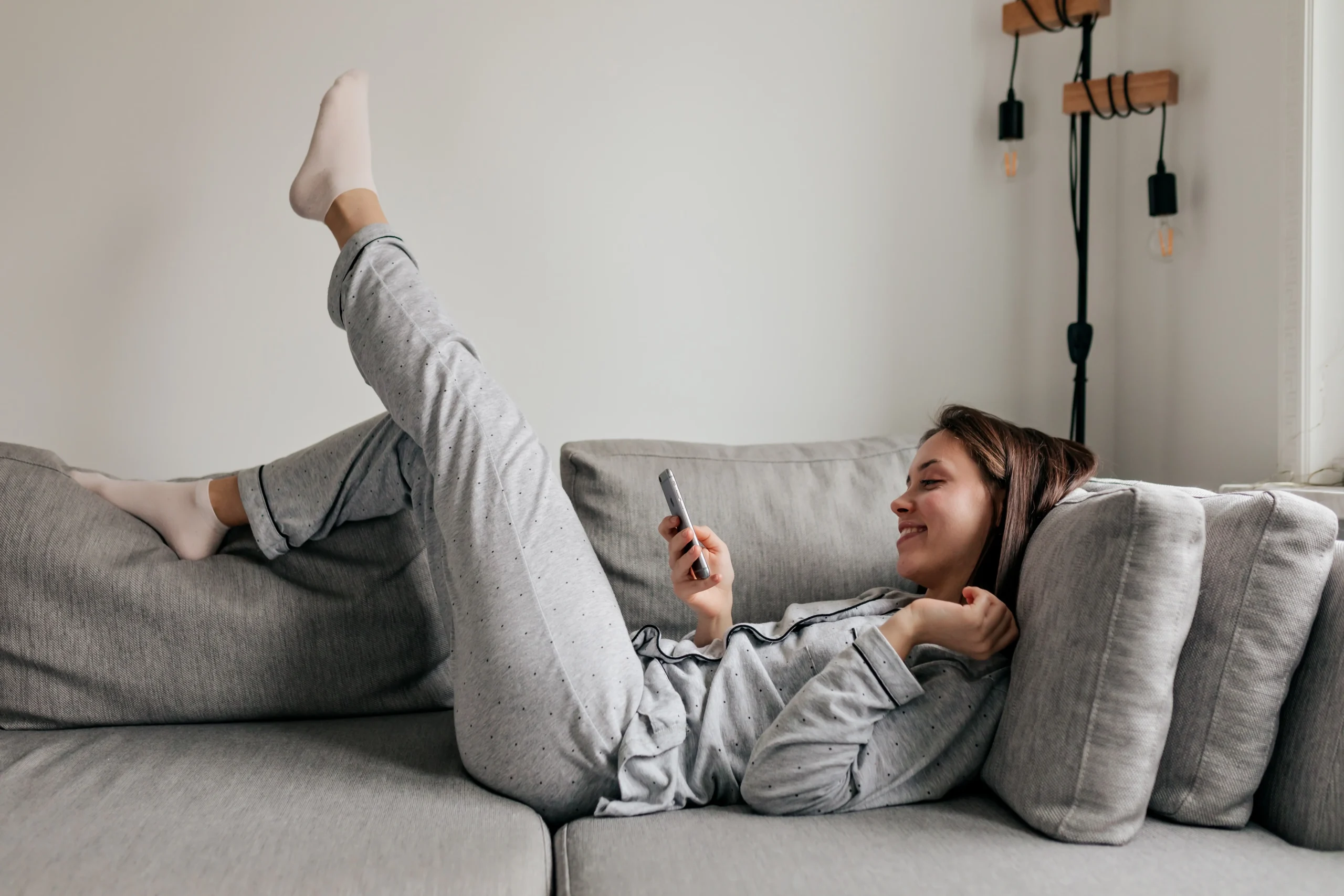 Žena leží na gauči s telefonem v ruce