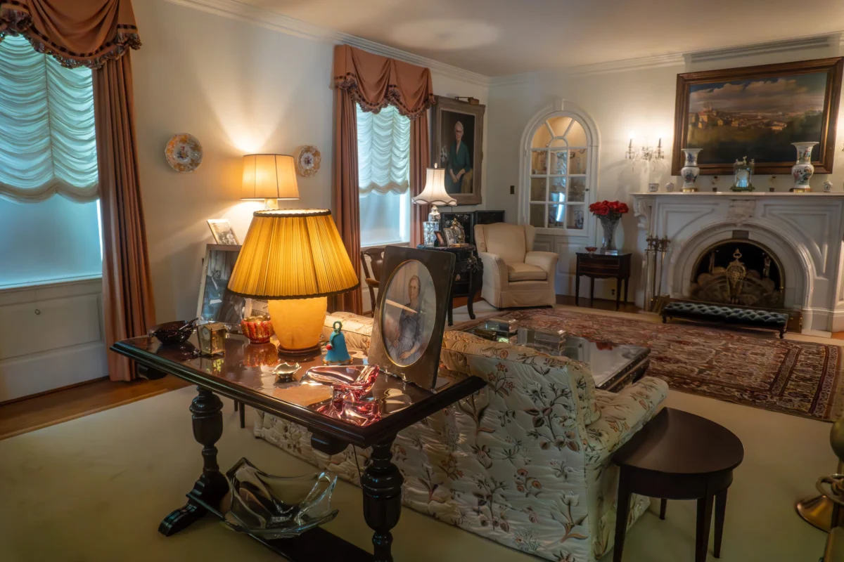 Elegant traditional living room with a marble fireplace, framed portrait, and floral upholstered seating under warm lamps and draped windows.