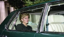Woman with short blonde hair and pearl necklace sits in the passenger seat of a dark green car with beige interior and window down.