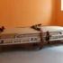 A hospital gurney with a beige mattress and brown straps sits in an empty orange-walled room by a window.