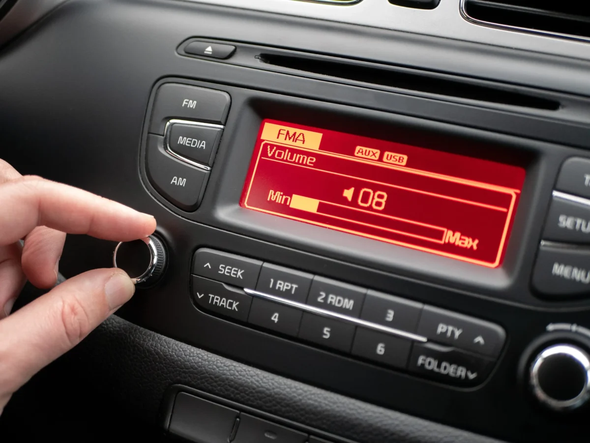 Close-up of a car stereo with FM/Media/AM buttons and a red display; a hand holds a metal key ring near the volume knob.