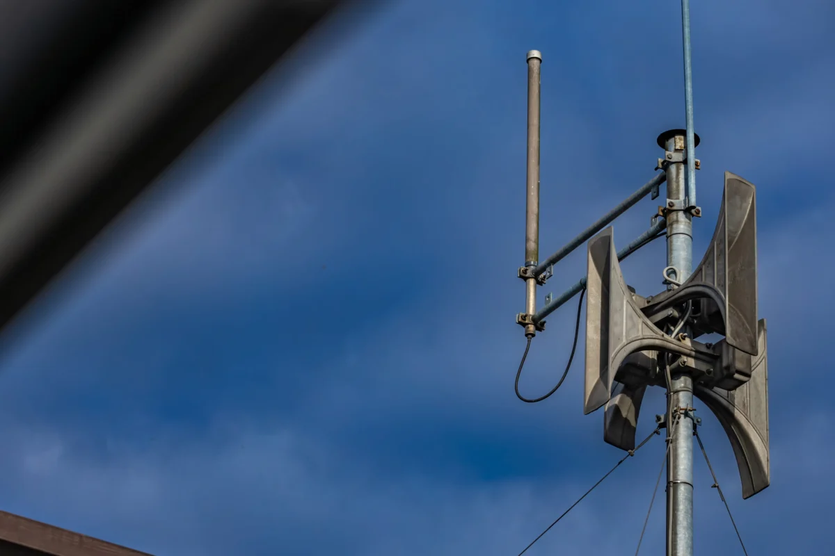 Metal utility pole section with clamps, cables and insulators against a clear blue sky.