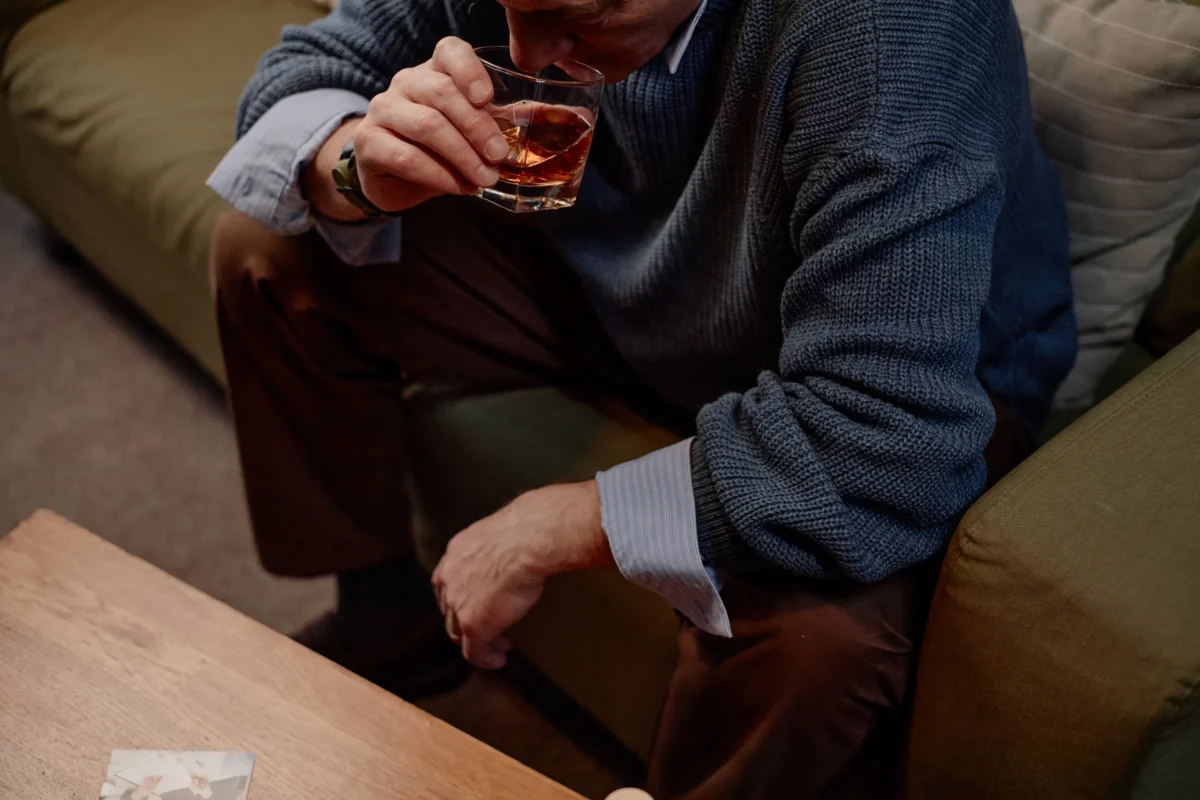Muž sedí s alkoholem na gauči.