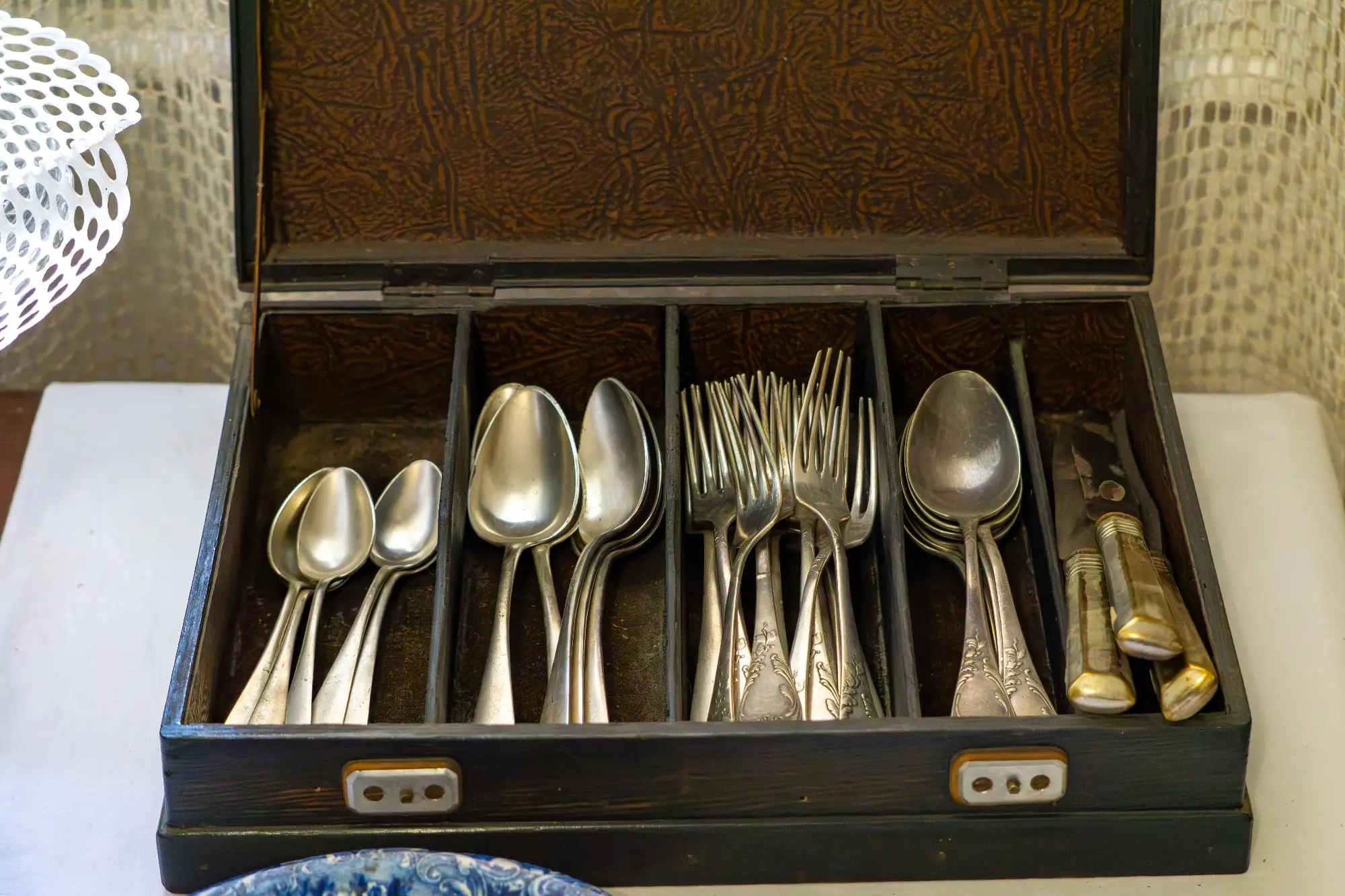 Open wooden cutlery box with neatly arranged silver spoons and forks in divided compartments.