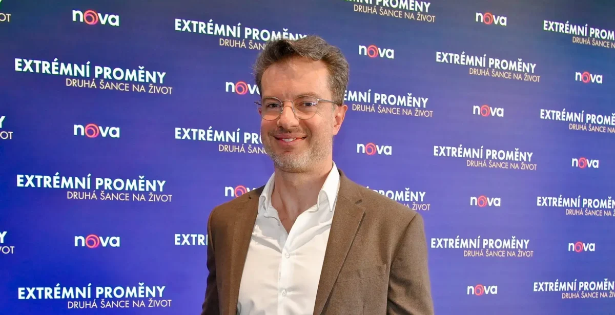 profimedia-1079279557 1 | TVGURU.cz Smiling man in a brown blazer and white shirt poses in front of a blue backdrop with Extrémní Promény and nova logos.