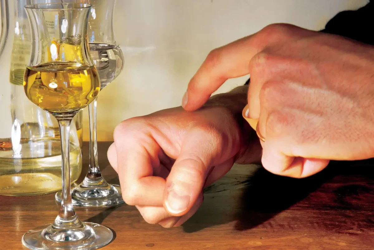 Close-up of hands wiping a wooden table with a small orange cloth beside two wine glasses and a bottle in the background.