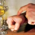 Close-up of hands wiping a wooden table with a small orange cloth beside two wine glasses and a bottle in the background.