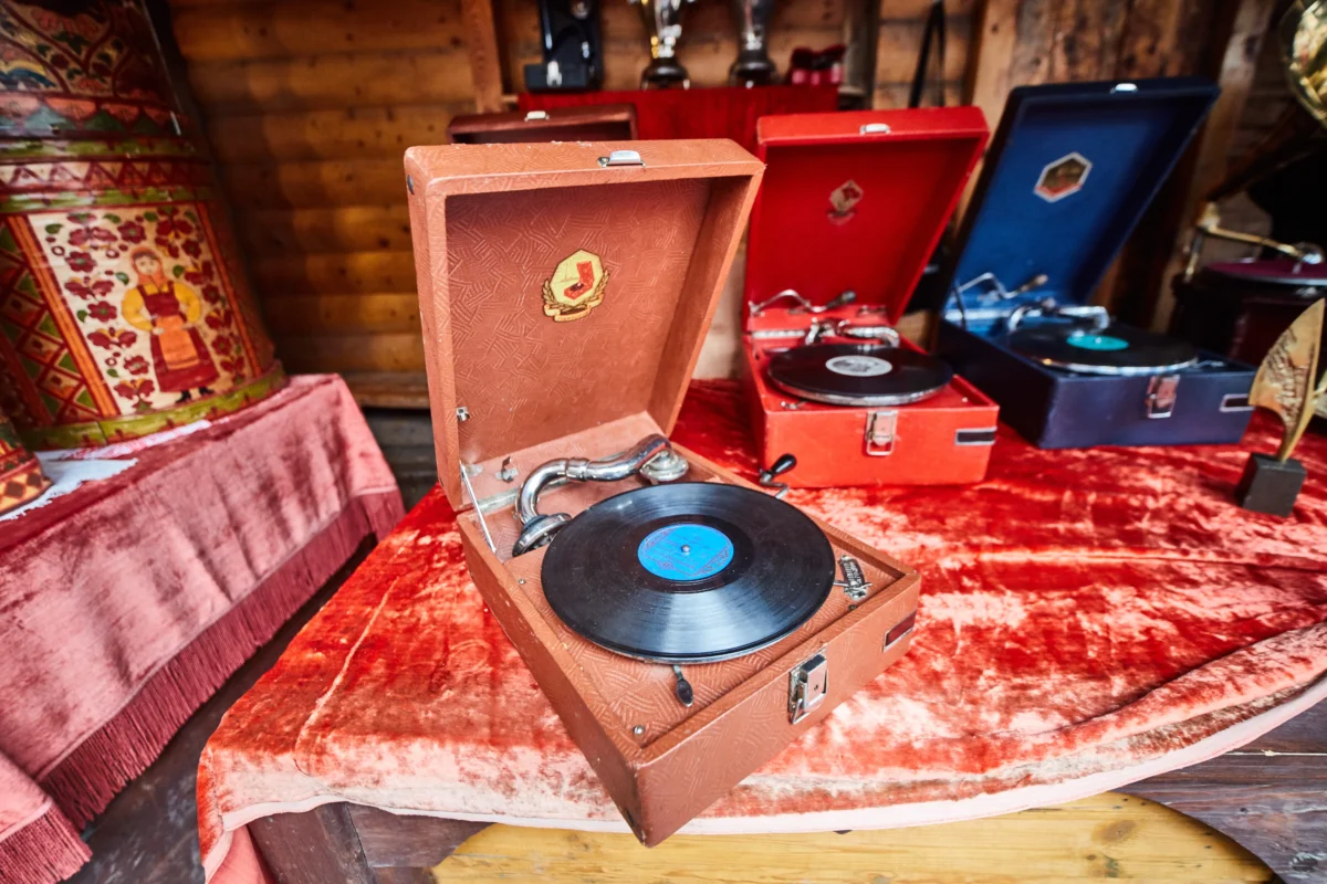 shutterstock_694017919 1 | TVGURU.cz Open brown vintage portable record player with a spinning vinyl on a red velvet table, wood cabin backdrop behind it.